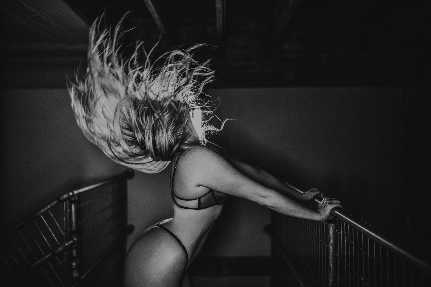 Black and white photo of a woman tossing her hair on a staircase railing.