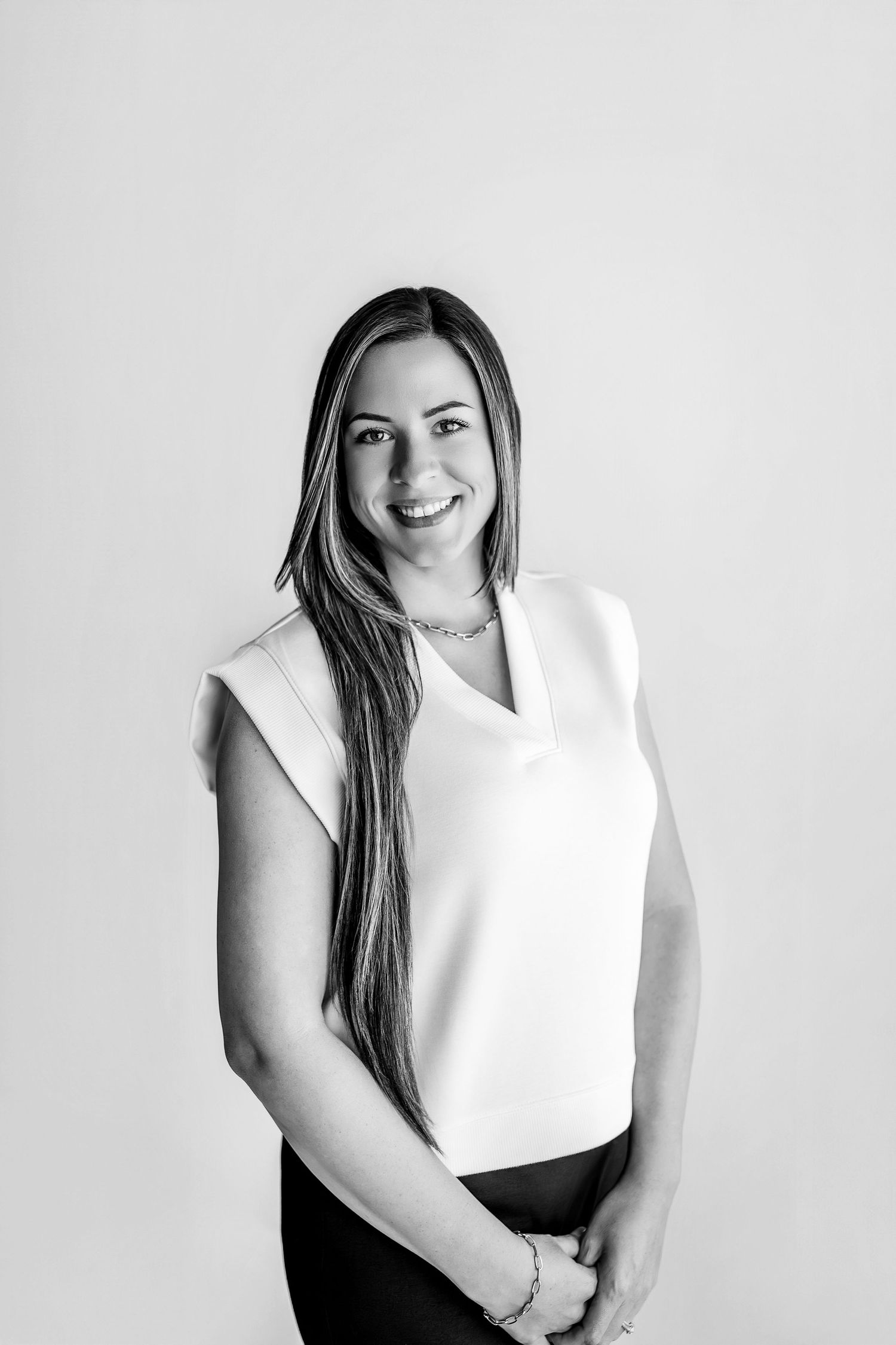 Black and white portrait of a smiling woman with long hair wearing a white sleeveless top and dark pants.