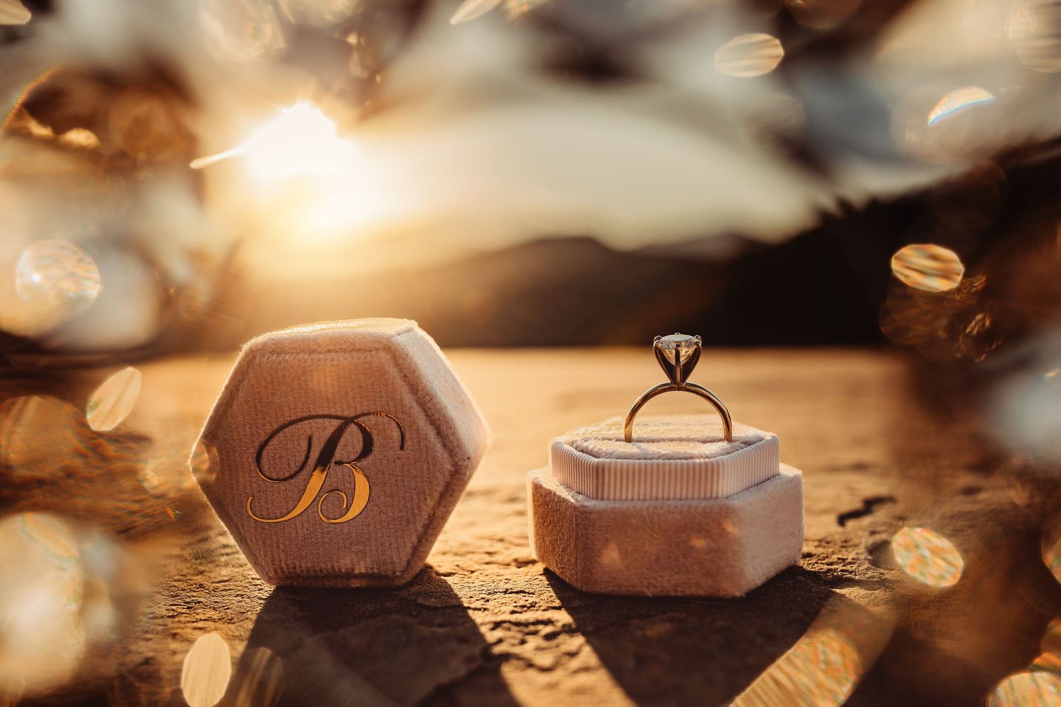 Diamond engagement ring displayed beside a monogrammed hexagonal velvet ring box in golden sunset light.