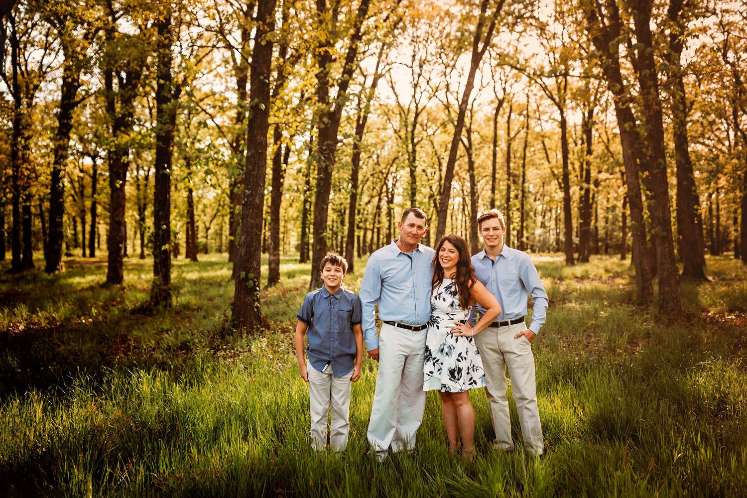 Family of four posing in a sunlit forest with golden autumn foliage during an outdoor portrait session.