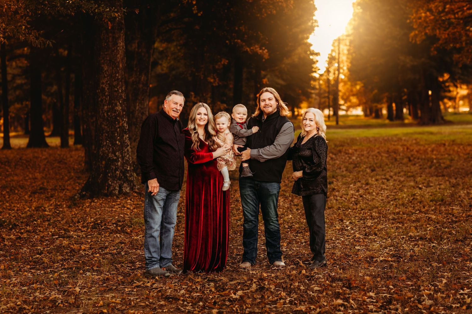 Family of five posing outdoors in autumn park with golden sunset light and colorful fall foliage backdrop.