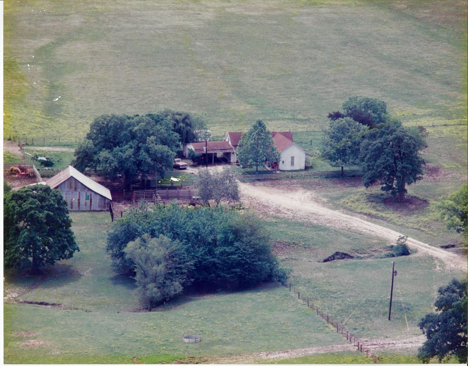A panoramic view of a rural countryside with scattered farmhouses and dirt roads winding through green pastures.
