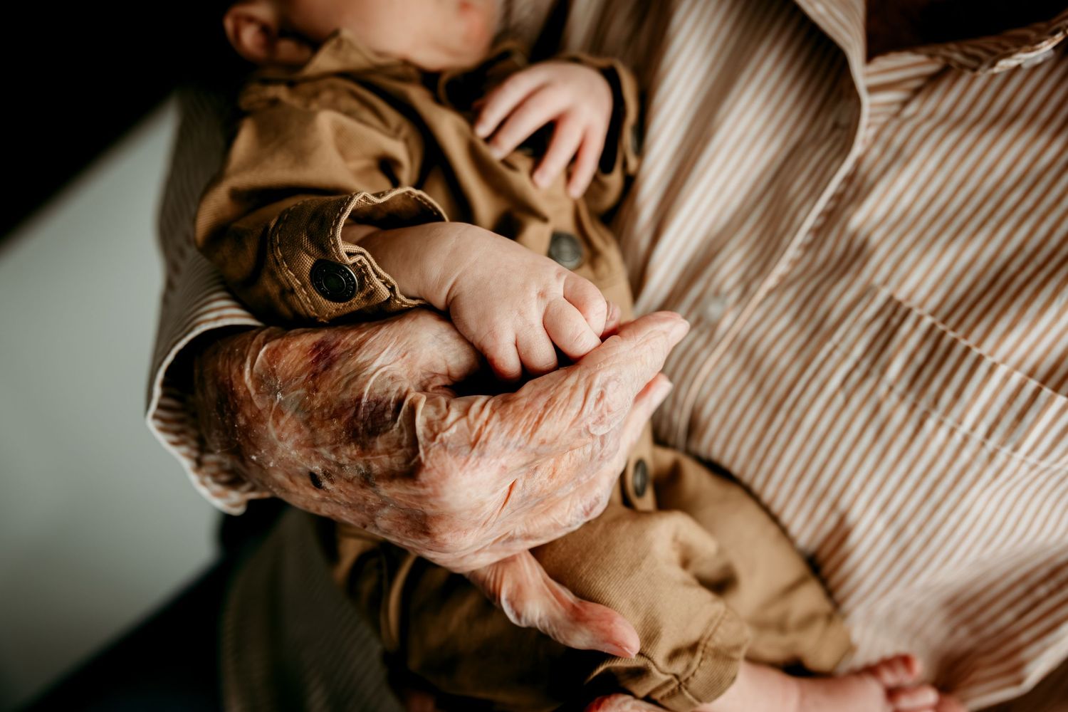 Elderly hands gently holding a newborn baby's tiny hand, showcasing a tender multigenerational moment.
