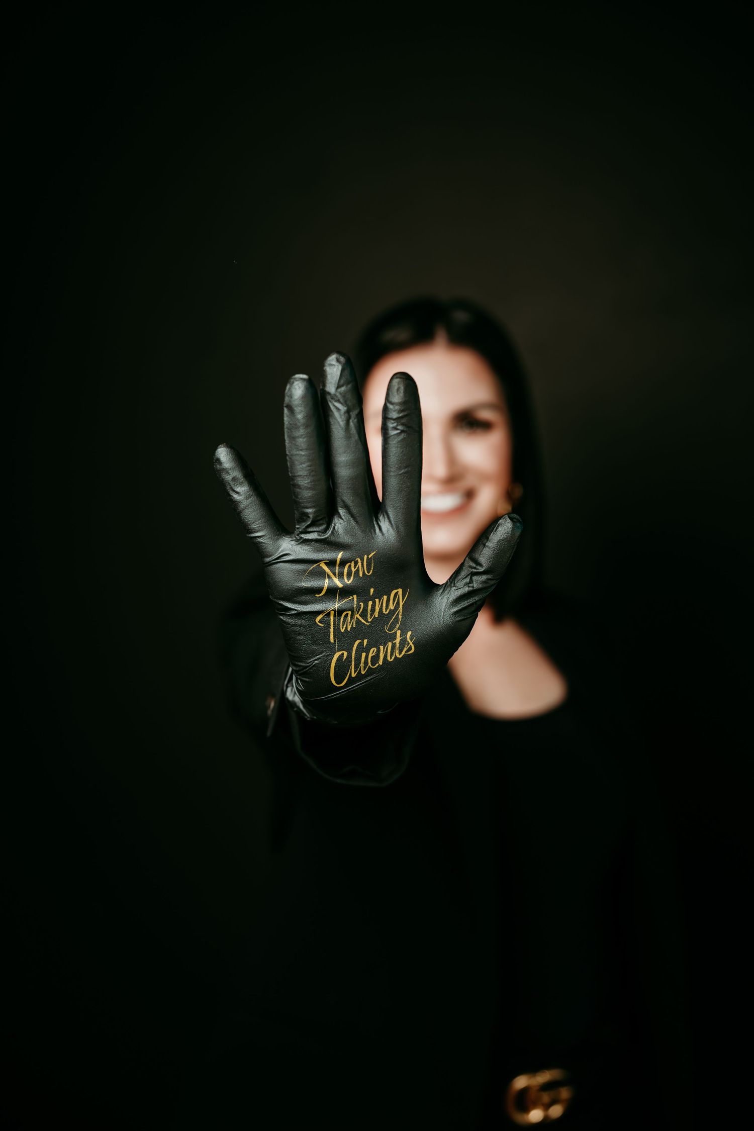 Smiling woman in black glove with gold text reading Now Taking Clients on dark background.