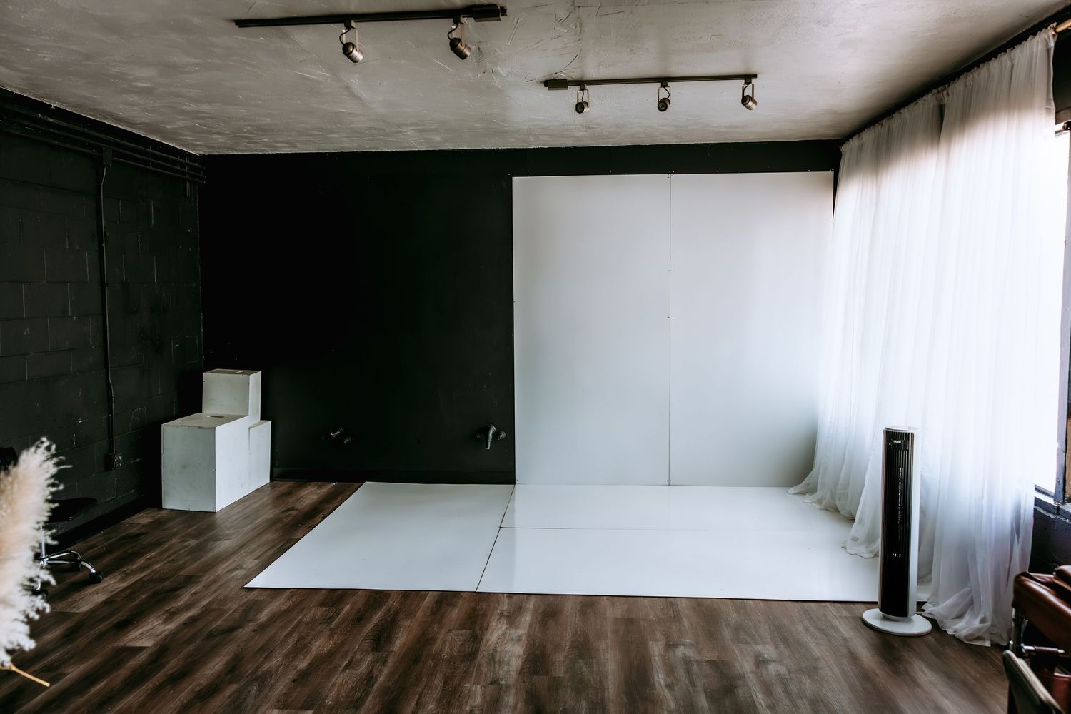 Modern photography studio with white backdrop, dark walls, hardwood floors, and track lighting.