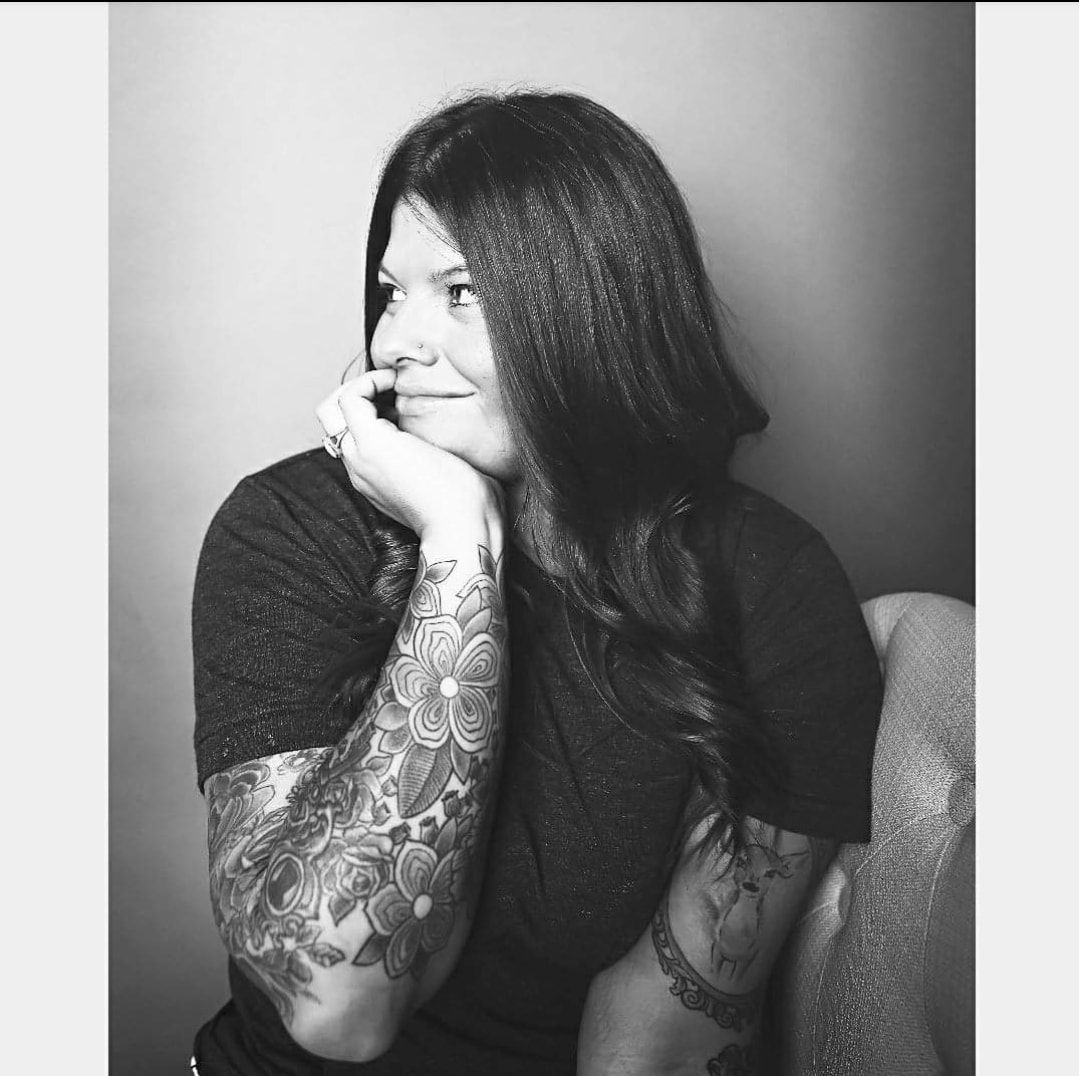 Black and white portrait series showing person with long dark hair and tattoos in contemplative poses against plain backdrop.