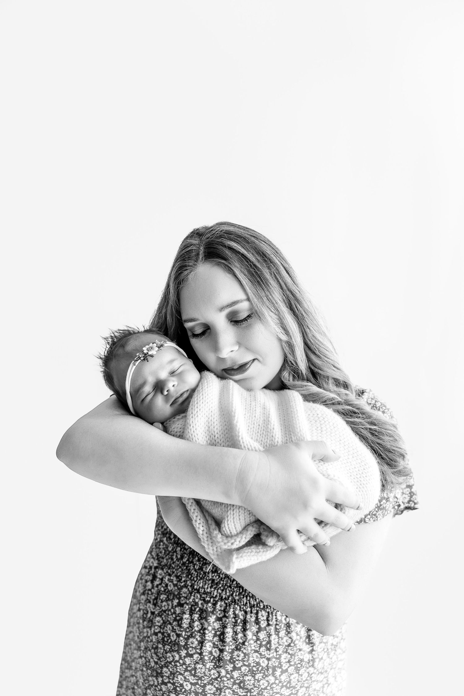 Black and white photo of a young mother tenderly cradling her sleeping newborn baby wrapped in a soft blanket.