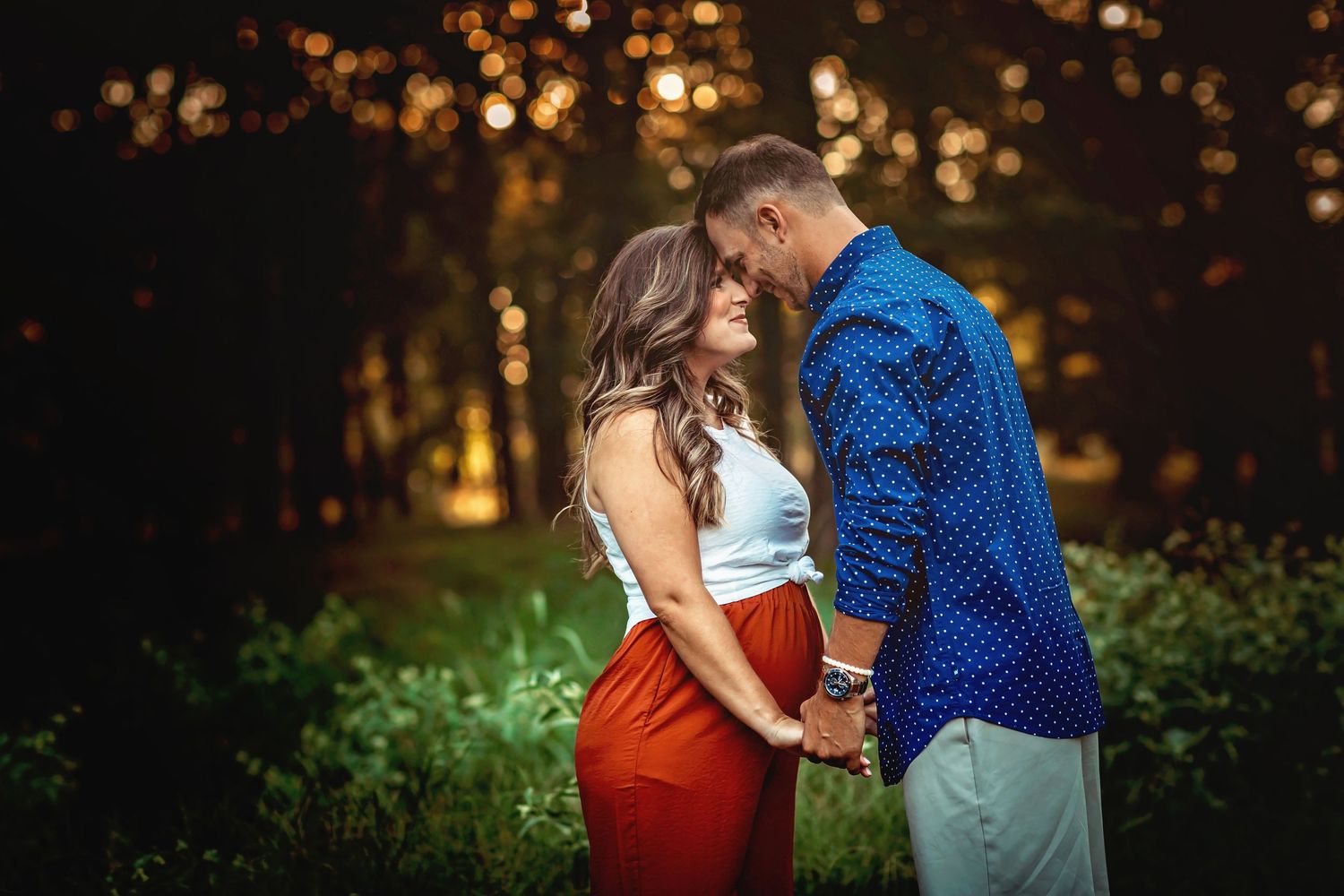 Couple sharing a romantic moment outdoors at dusk, woman in red skirt and white top, man in blue polka dot shirt.