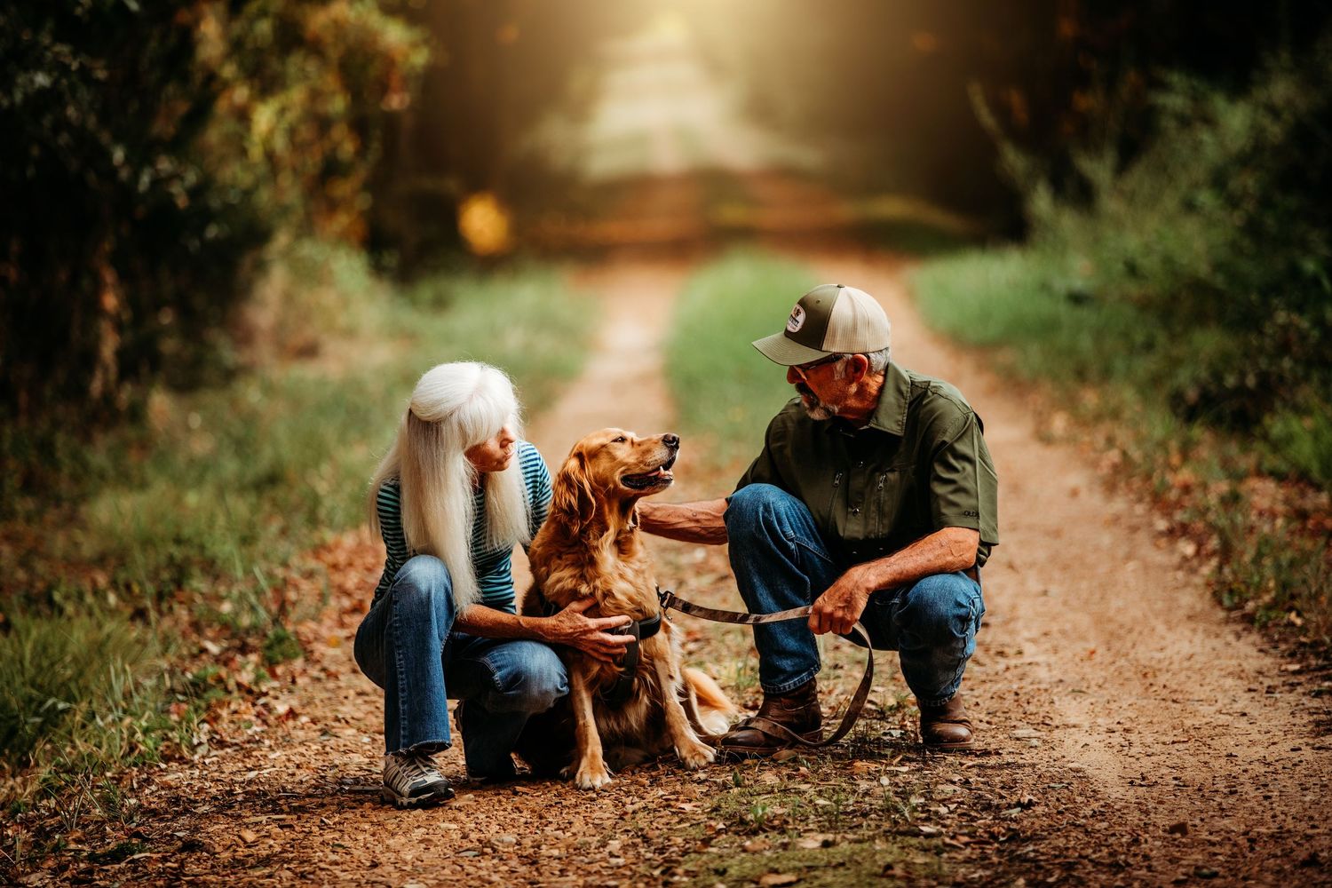 A family and dog enjoying a moment together on a fall path with golden light.