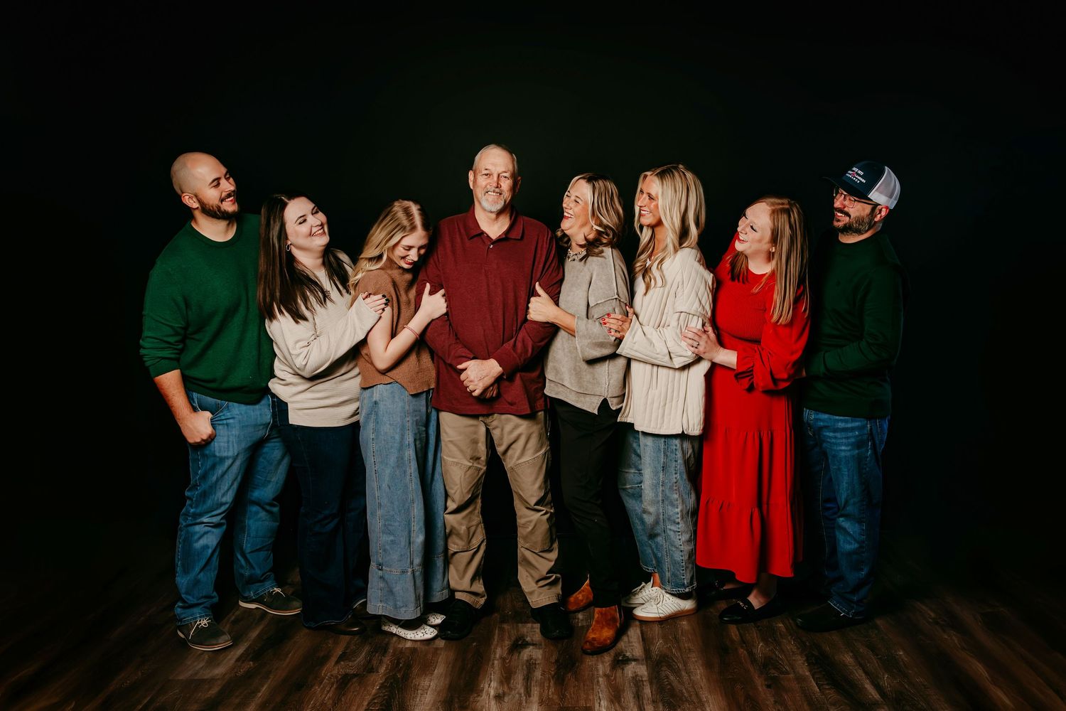 A joyful family of eight poses together laughing in a professional studio portrait against a dark background.