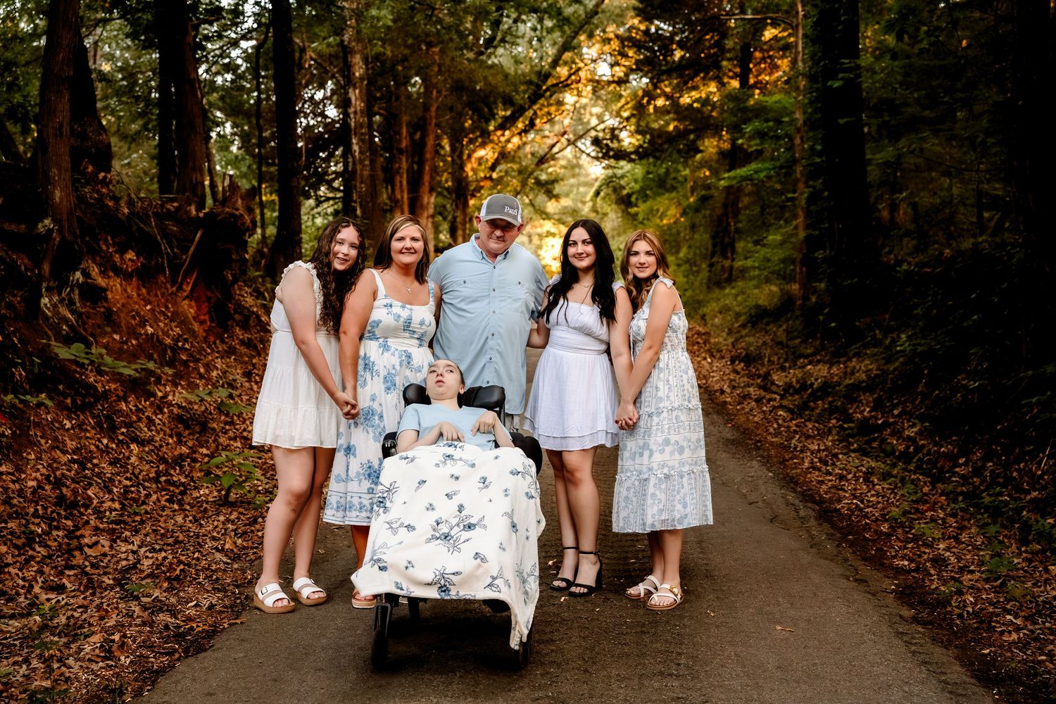 Family of six posing on a tree-lined path in autumn, with parents and children surrounding a baby stroller.