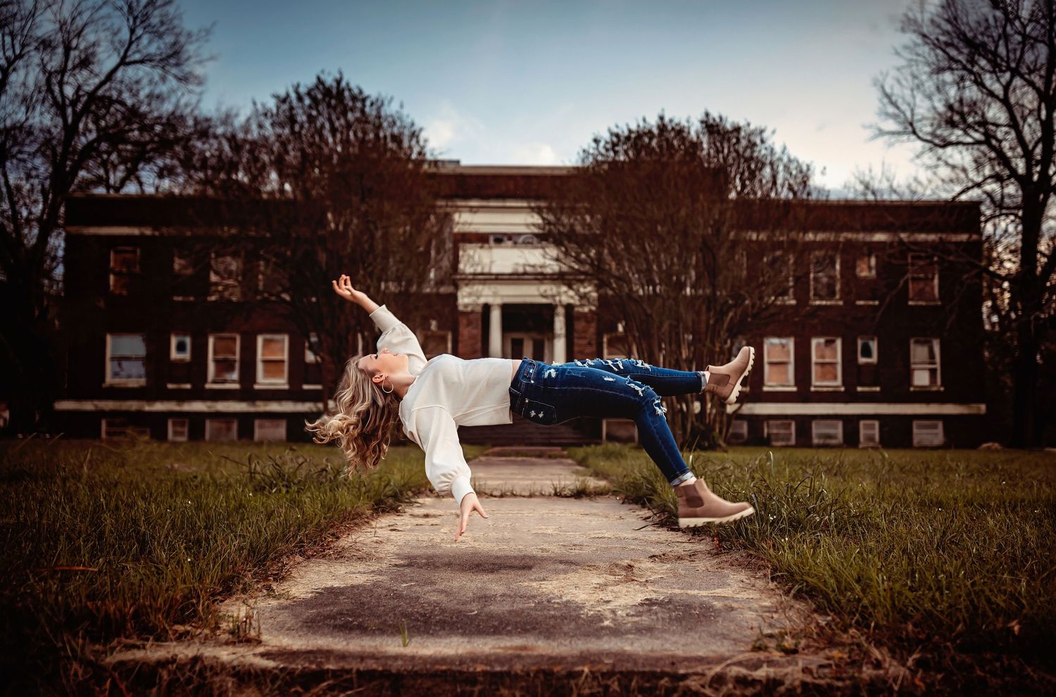 Woman levitating horizontally outdoors in front of a historic brick building, wearing jeans and white top.