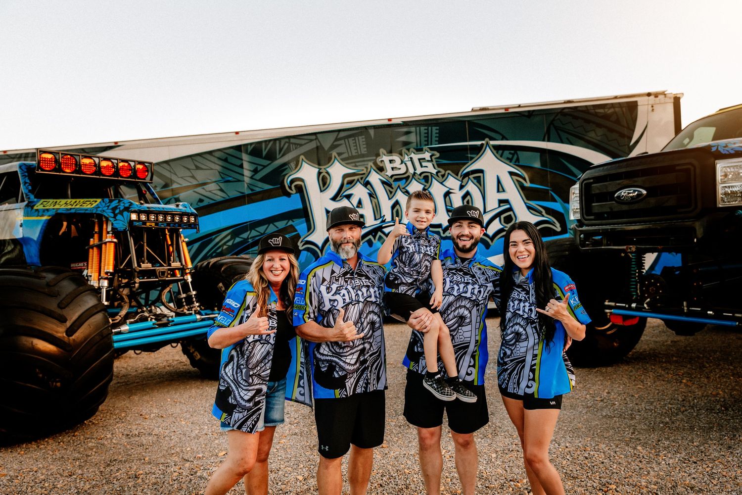 Group of people wearing blue tie-dye shirts stand in front of a graffiti-covered wall during a gathering.