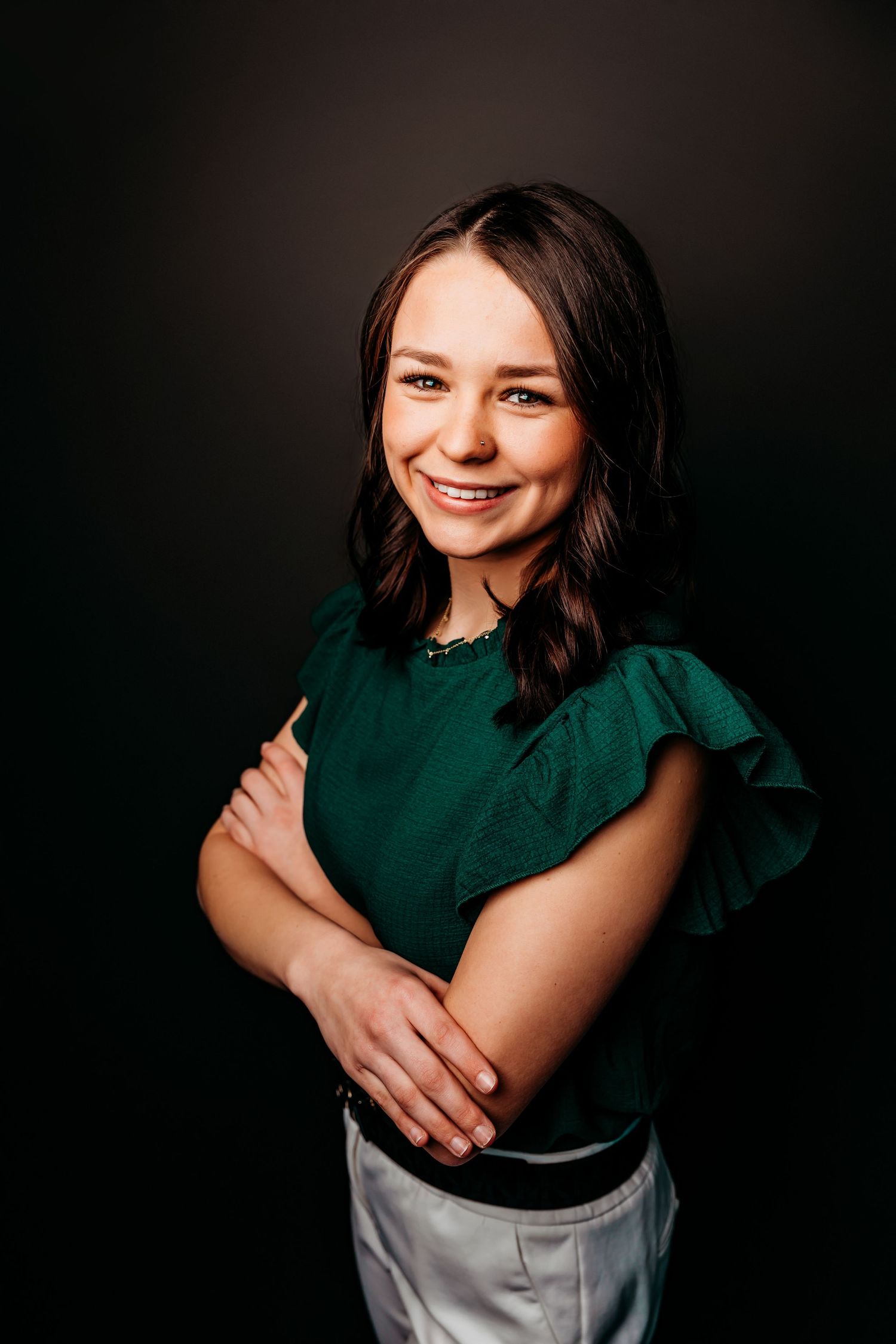 Studio portrait against dark background featuring emerald green top and natural poses.