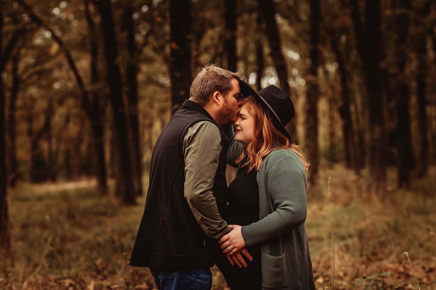 Couple sharing a romantic moment in an autumn forest, woman wearing a black hat and green cardigan.