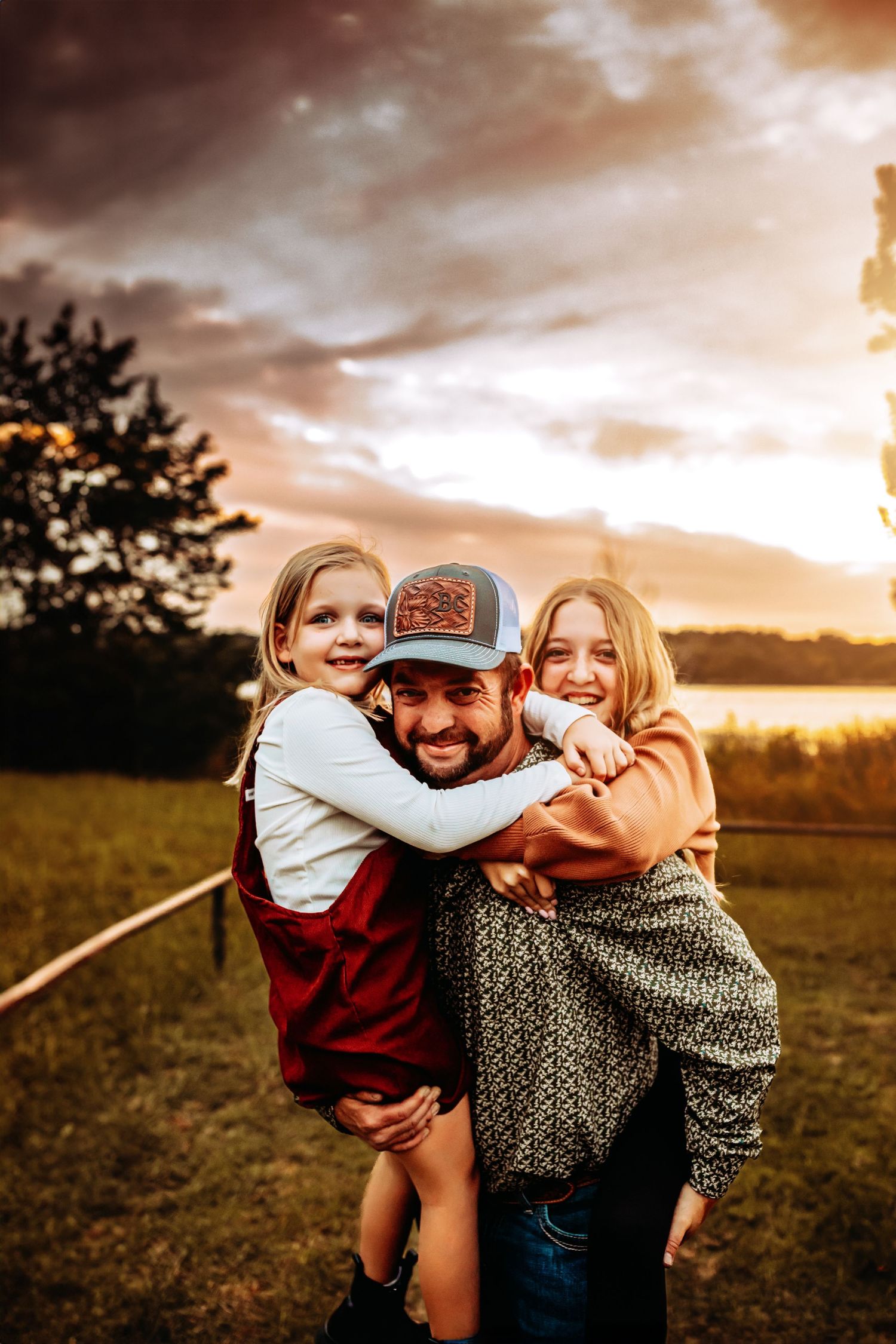 A playful family moment captured during golden hour in a field with dramatic sunset clouds.