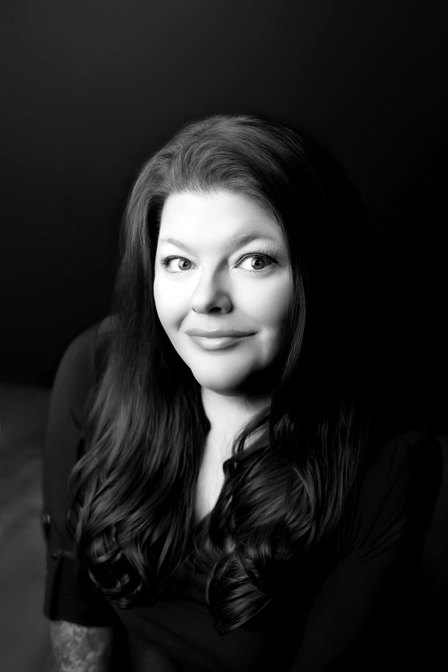Black and white portrait of a woman with long wavy hair smiling softly against a dark background.