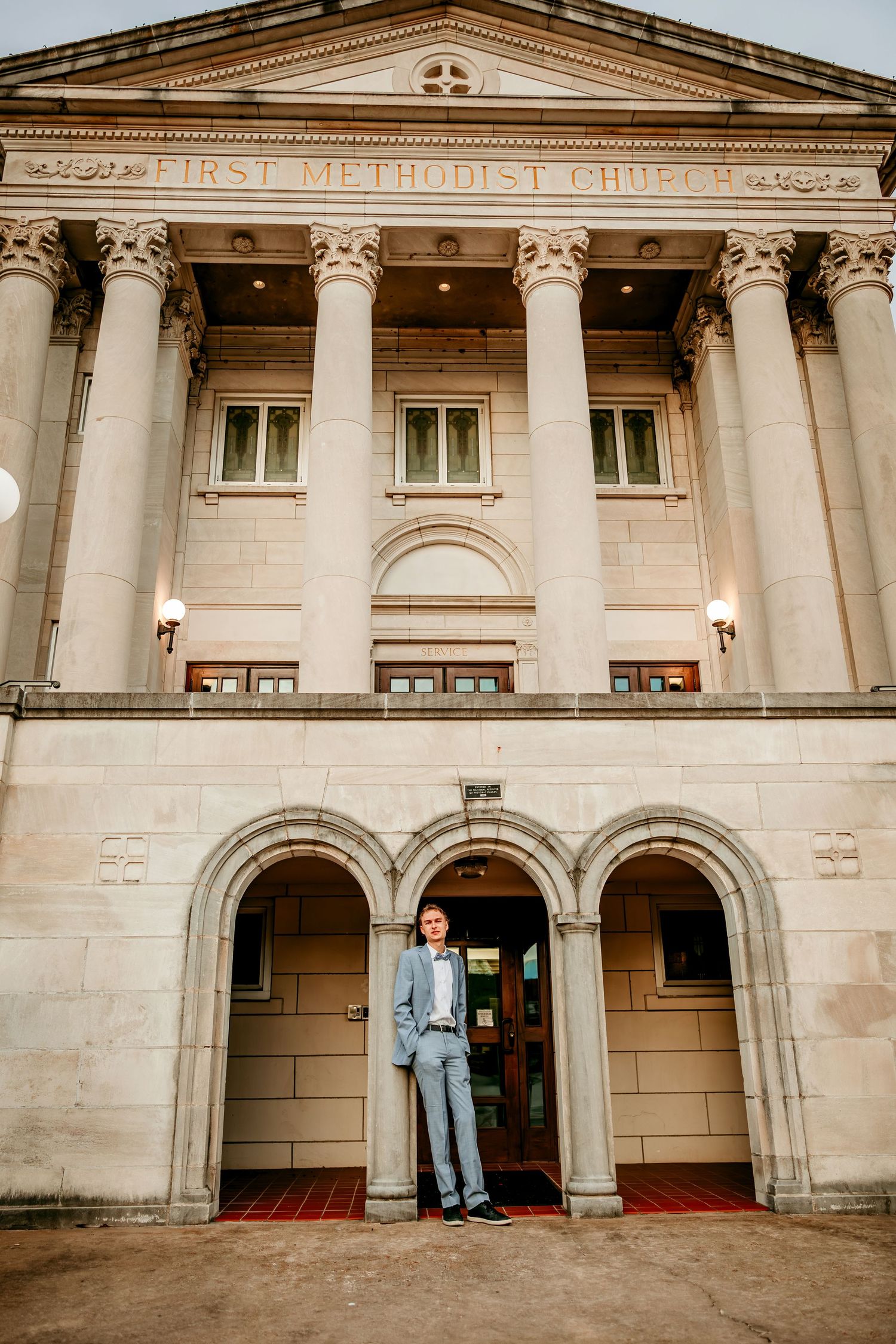 Man in suit standing at entrance of First Methodist Church with grand columns and arched doorways.