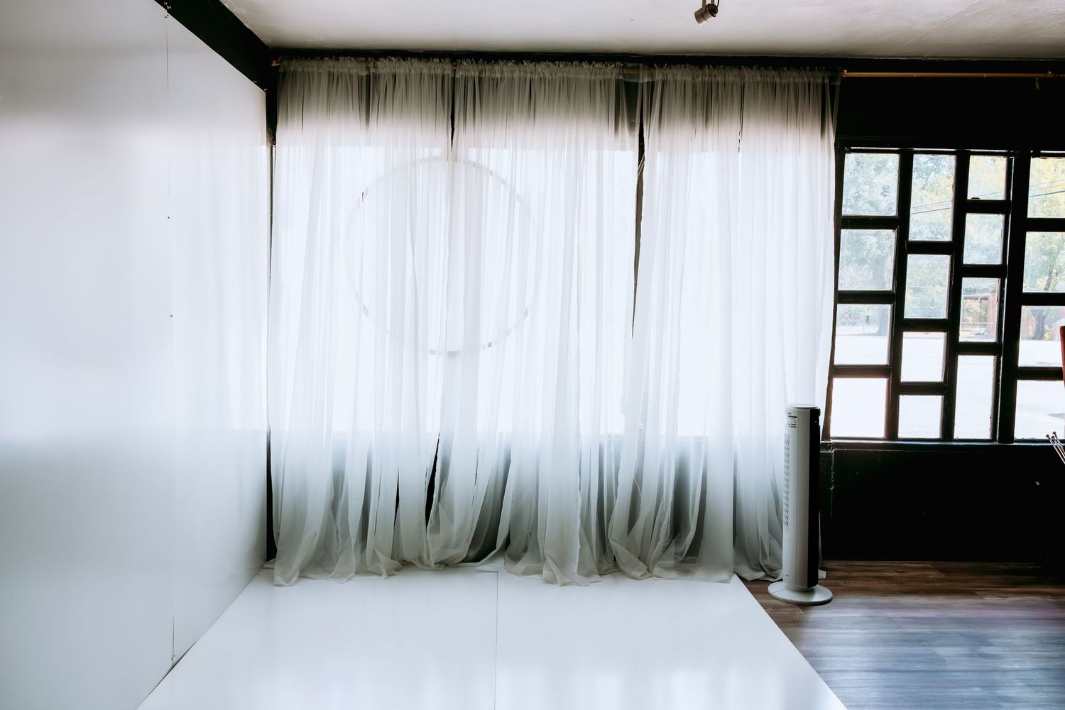 Sheer white curtains draped elegantly in a minimalist room with hardwood floors and a wooden window panel.