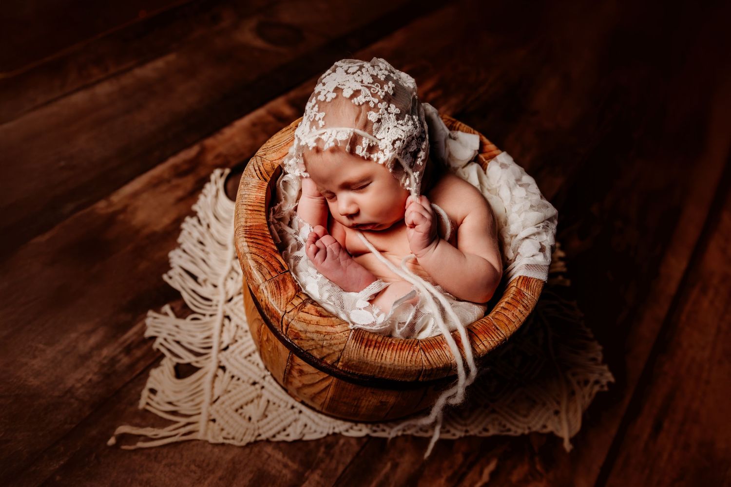 Sleeping newborn baby wrapped in white fabric lies peacefully in rustic wooden basket on dark background in a Paris, Texas Studio.