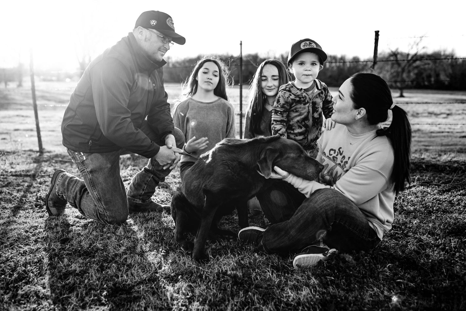 Black and white photo of a family with children petting a young calf together outdoors on a farm.