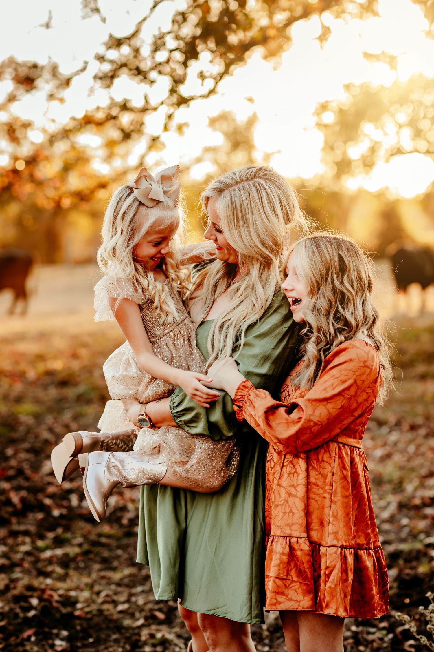 Children in green and orange dresses play together in autumn leaves during golden hour sunset.