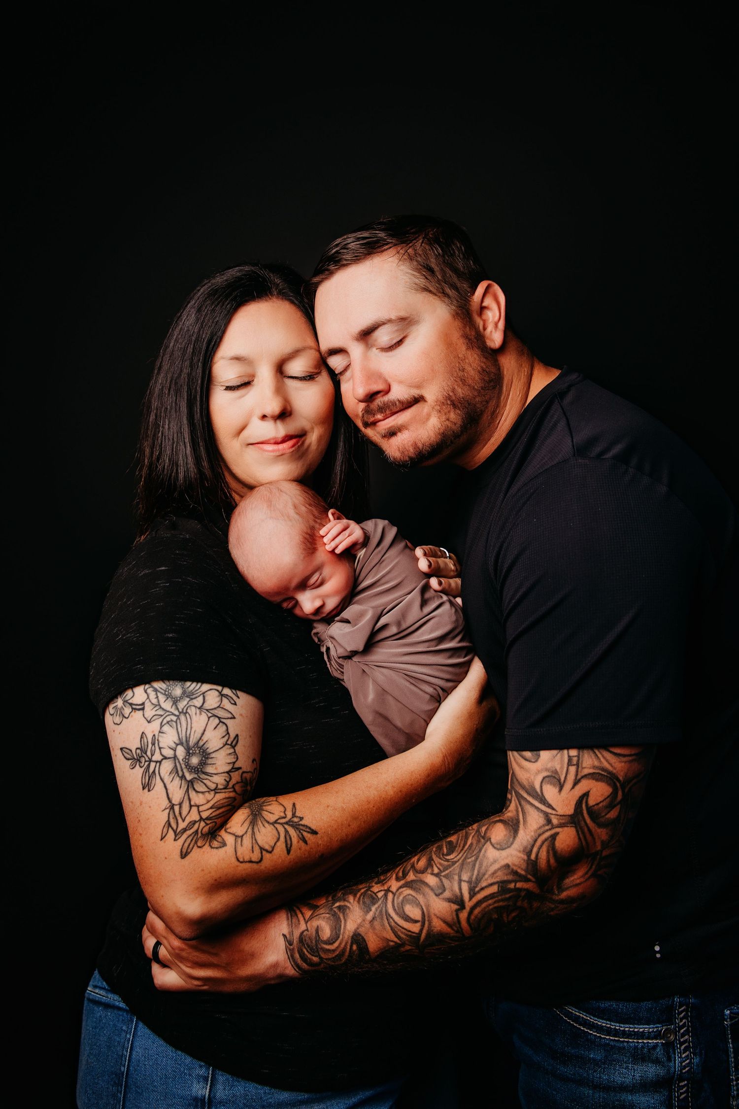 Intimate family portrait against dark background showcasing tattoo art and tender embraces.