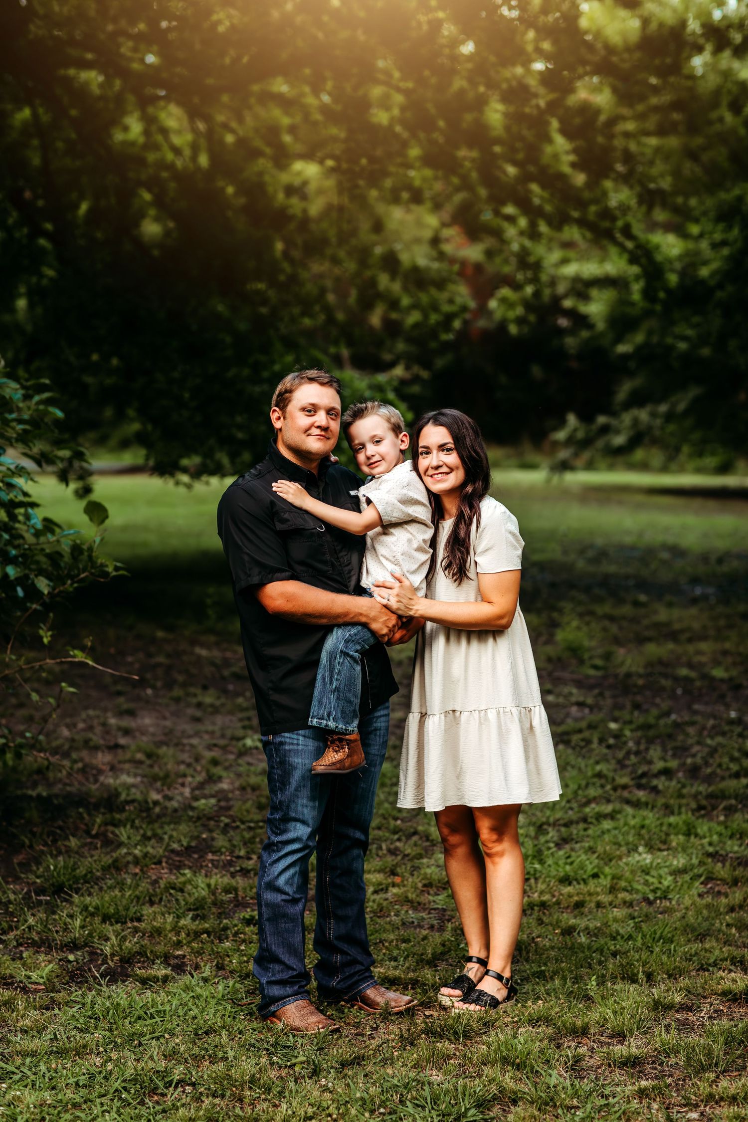 Three people share joyful moments together in a sunlit grassy outdoor setting.