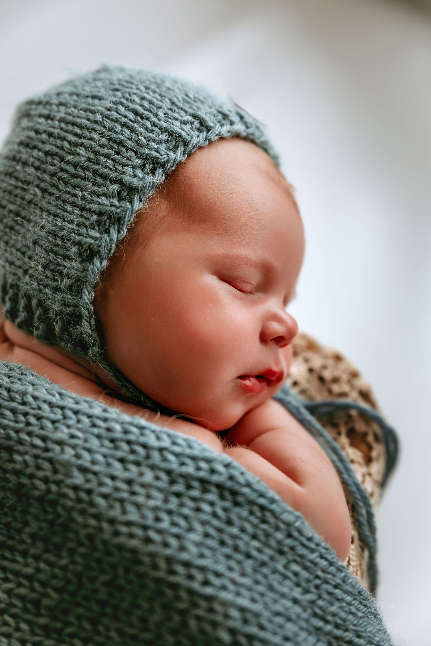 Peaceful newborn baby sleeping wrapped in a soft teal knit blanket and matching bonnet.