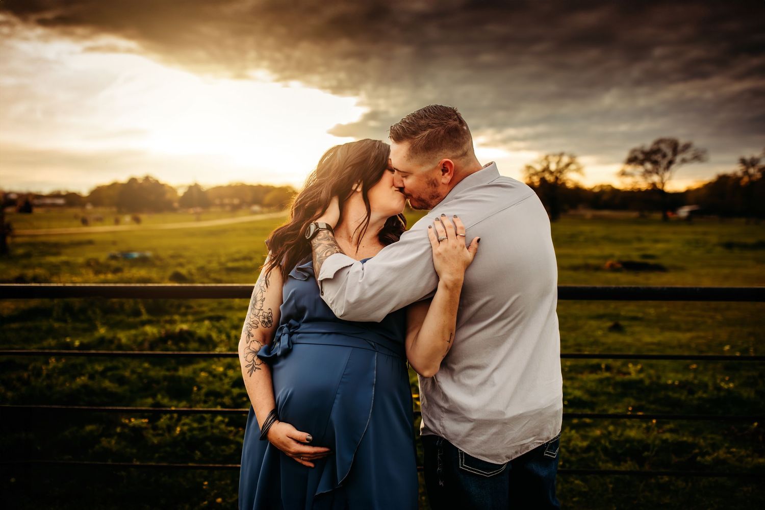 Romantic couple embraces in golden sunlit field during sunset creating intimate silhouettes against dramatic sky.