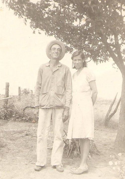 Vintage black and white photograph showing people standing outdoors near trees in casual attire.