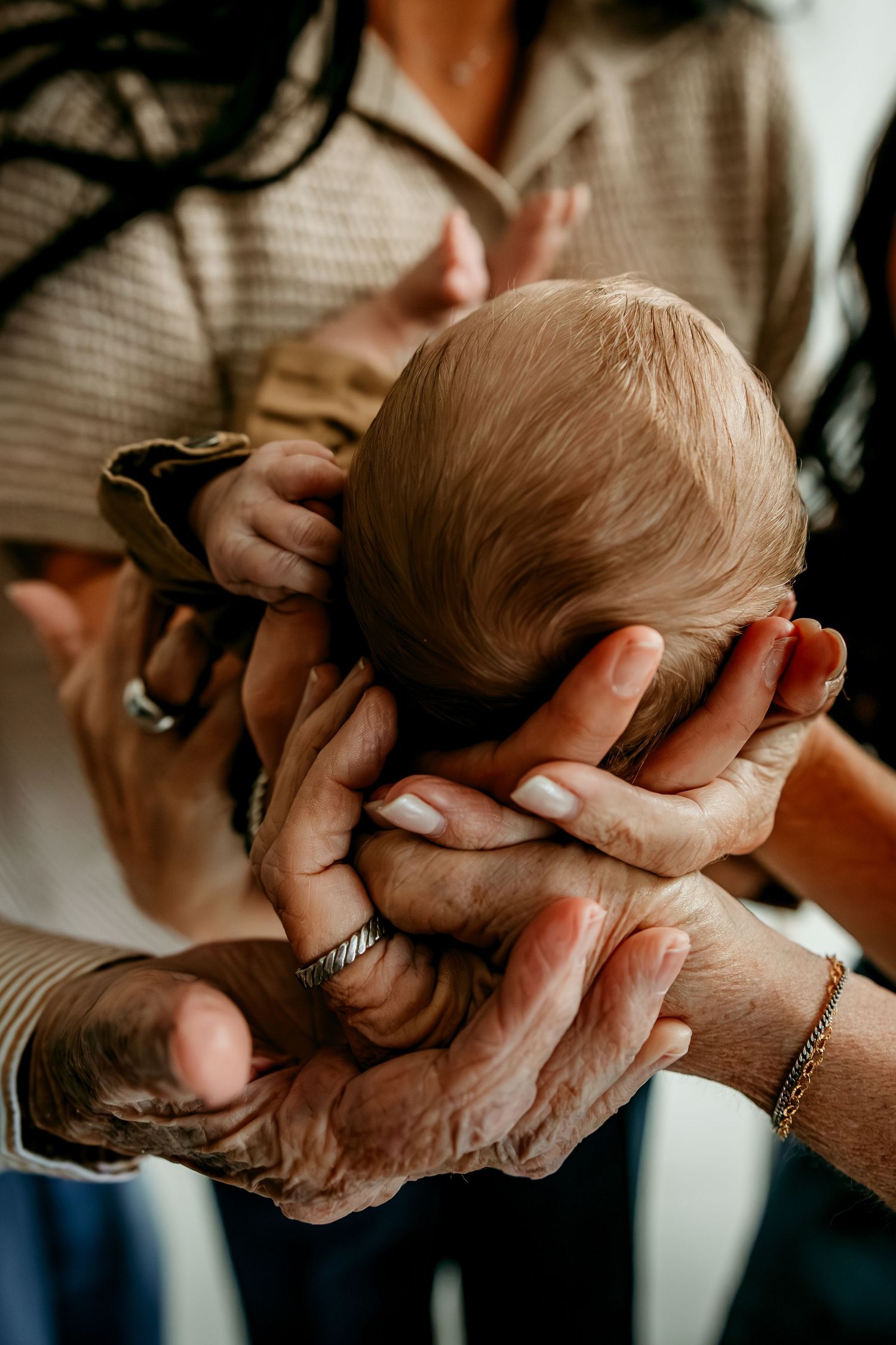 Multiple generations of hands cradling a newborn baby's head, symbolizing family love and new life.