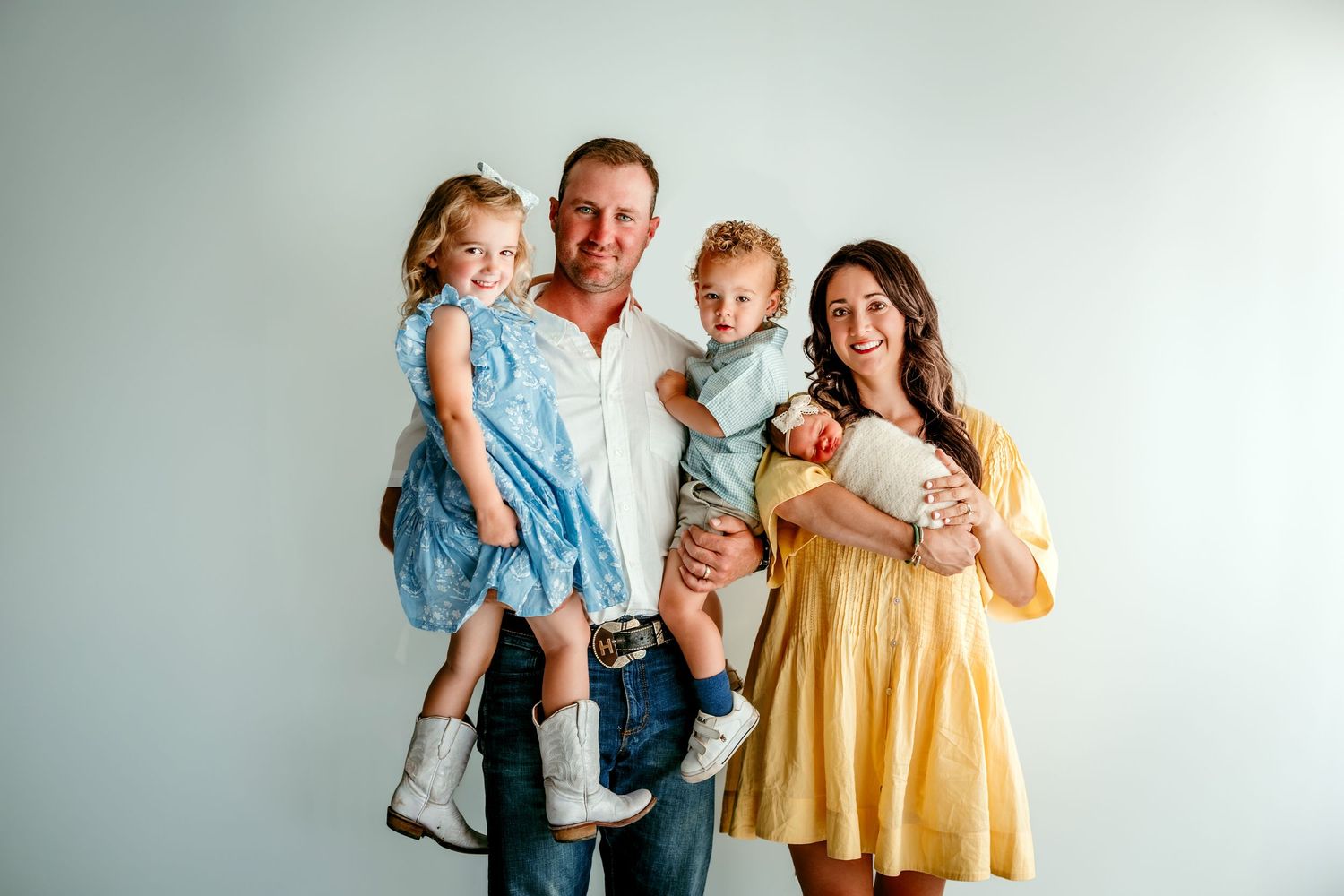Happy family of four posing for a studio portrait, parents holding two young children, wearing casual outfits.