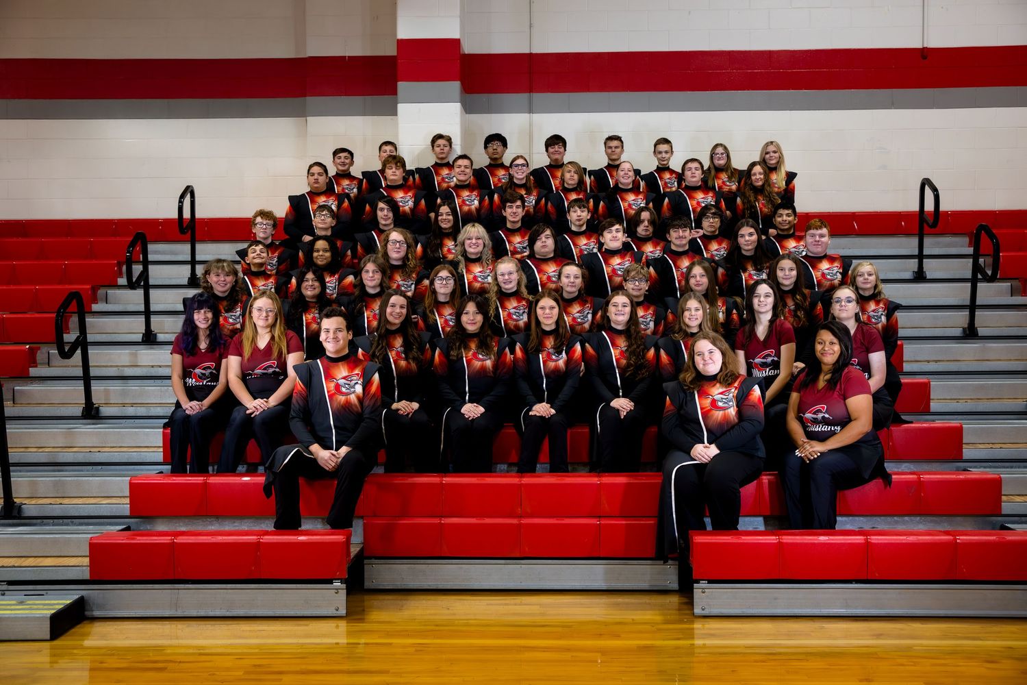 Large school group photo of students in red and black uniforms posed on gymnasium bleachers.