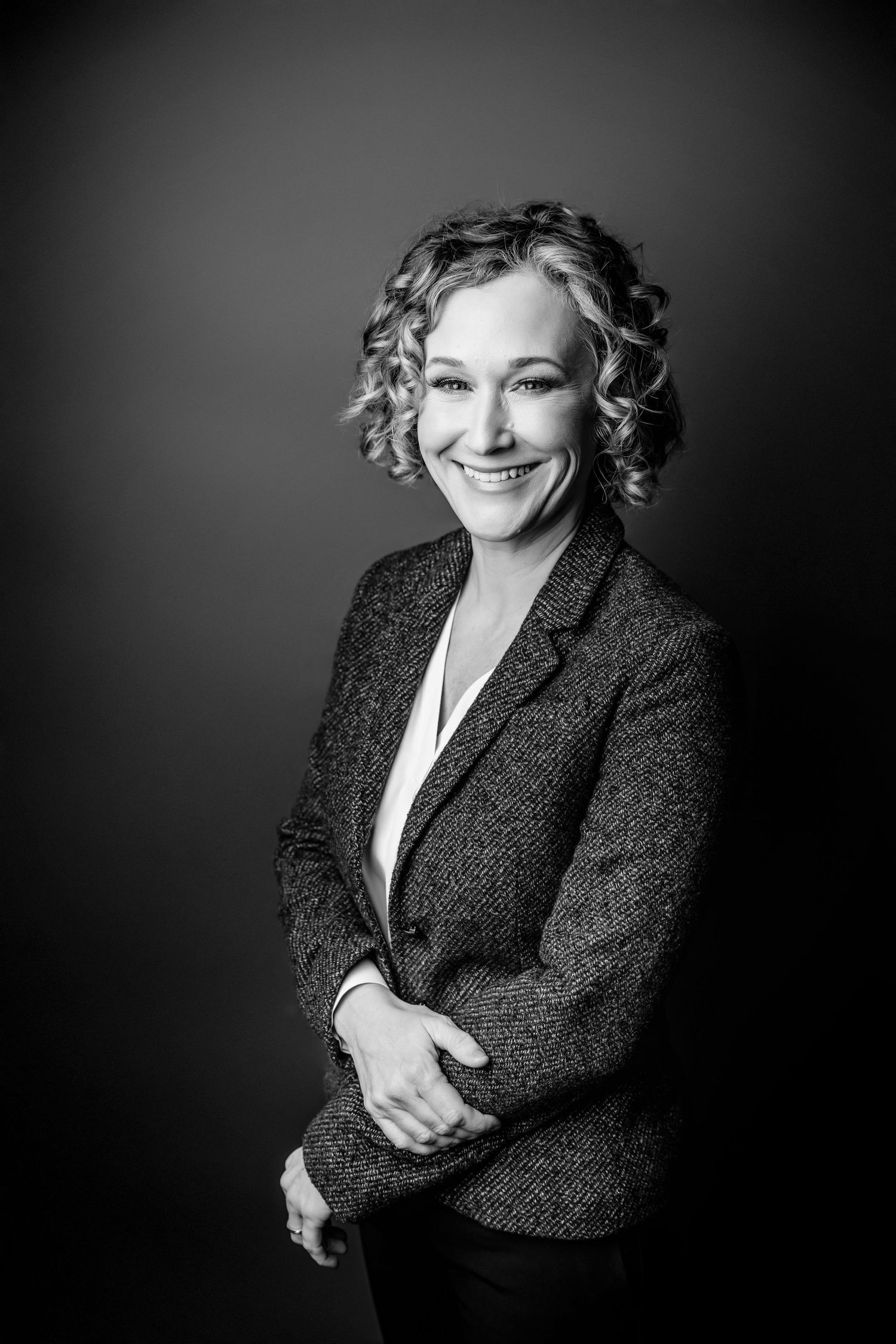 Professional black and white portrait of a smiling woman with curly hair wearing a blazer.