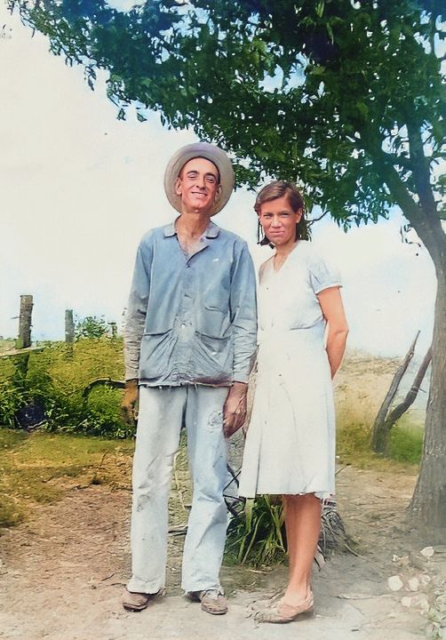 A vintage photograph from the 1940s shows two people standing together outdoors under a tree on a sunny day.