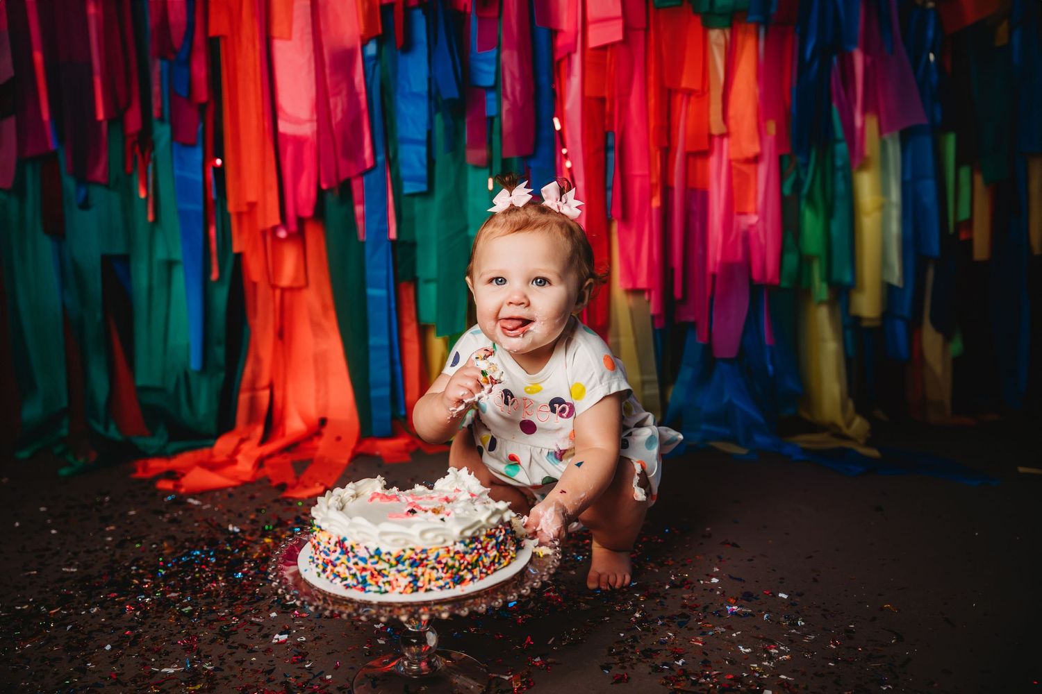 Colorful streamers create vibrant backdrop for cake smash photography session with bright decorations and festive setting.