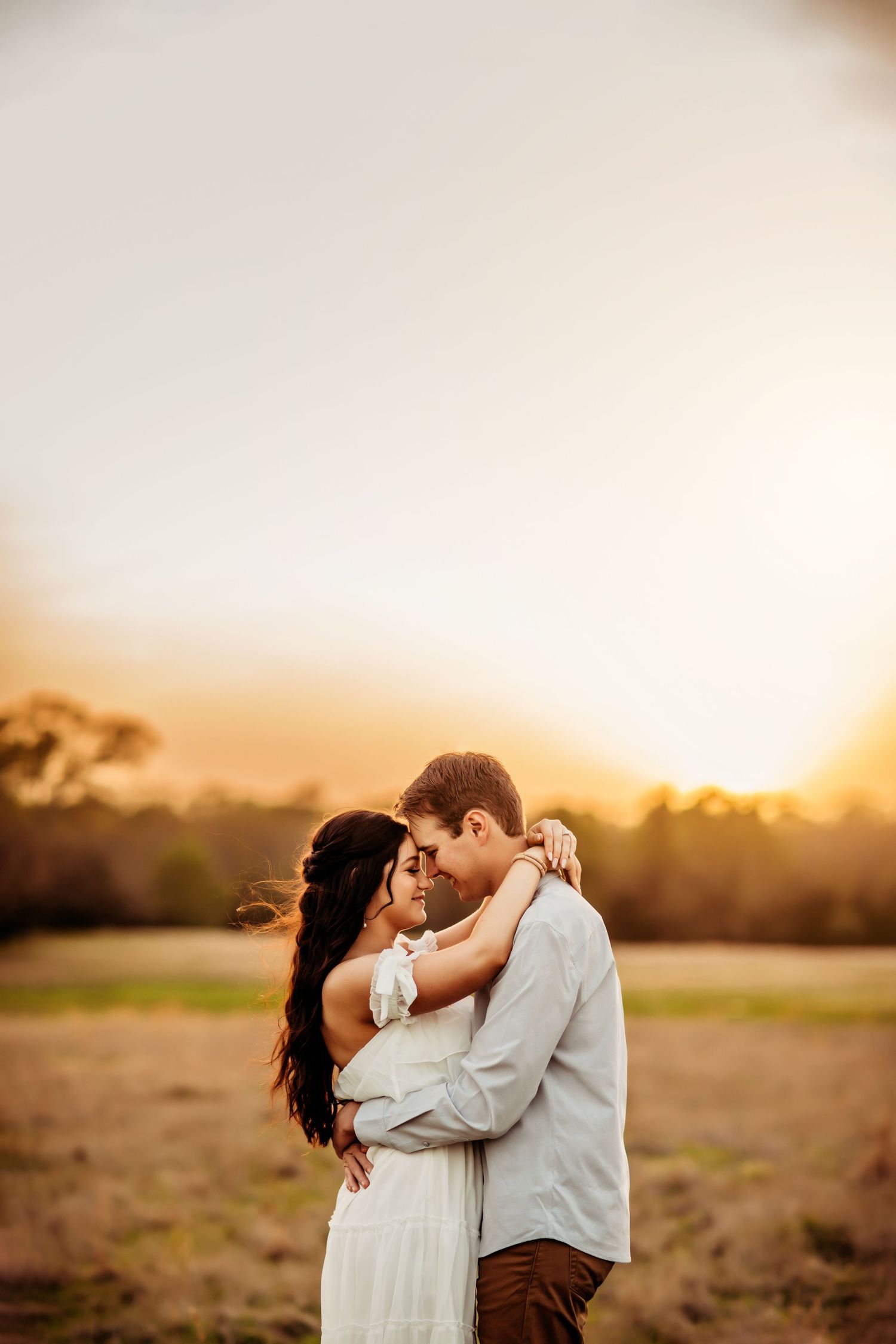 A romantic couple embracing in a field during golden hour sunset.