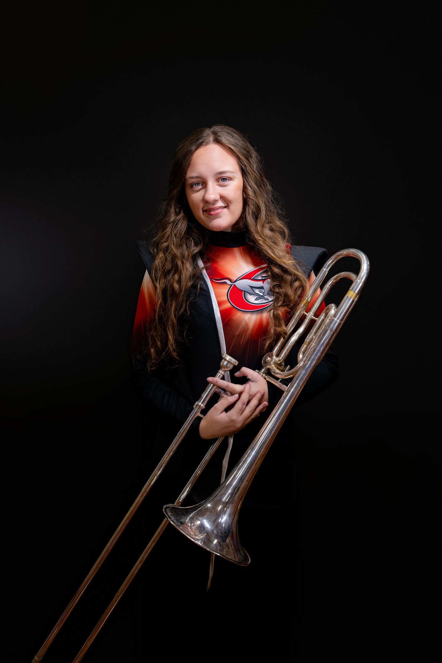Young woman in marching band uniform holding a trombone, posing against a dark background.