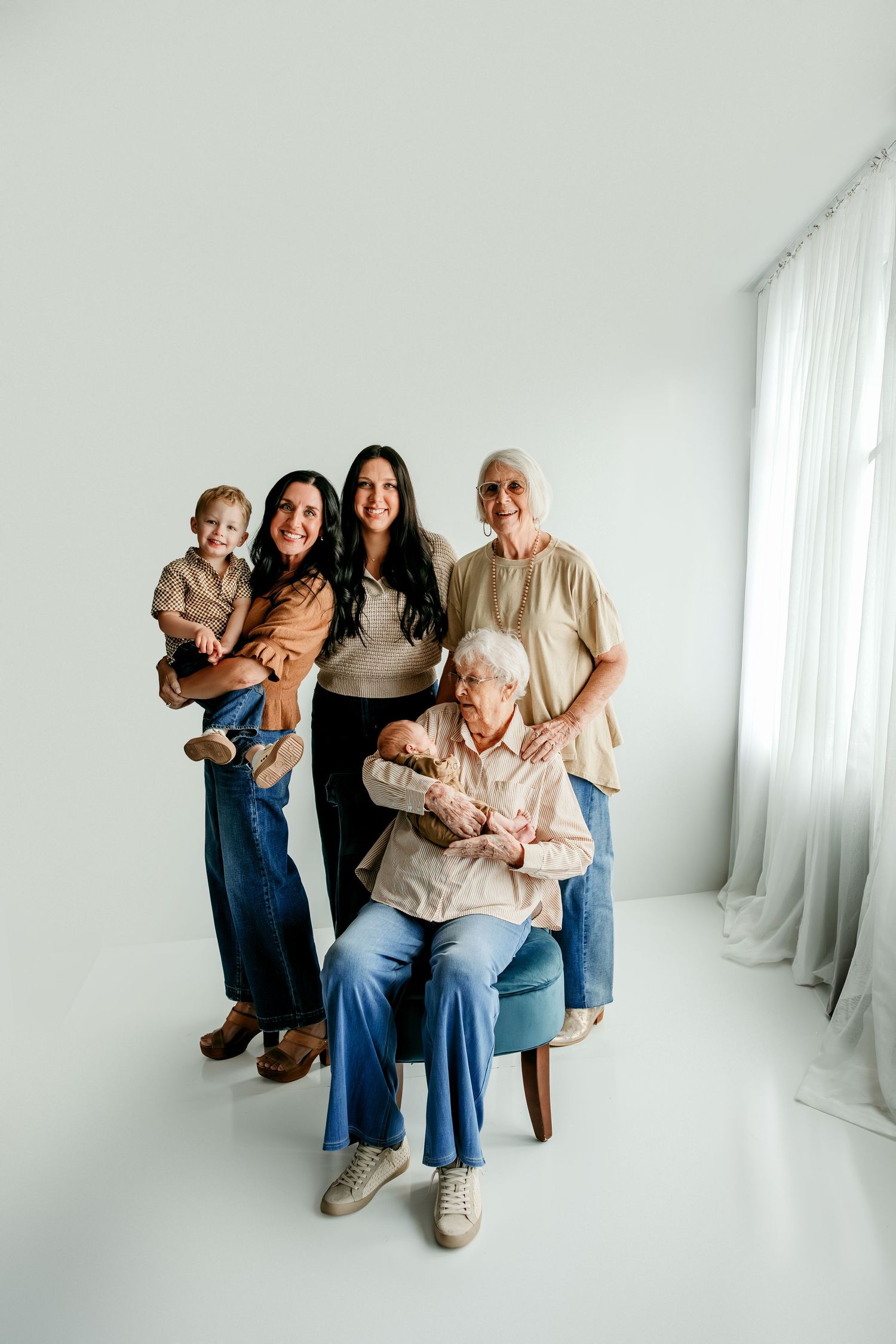 Multi-generational family portrait with five women and a toddler posing together in a bright white studio.