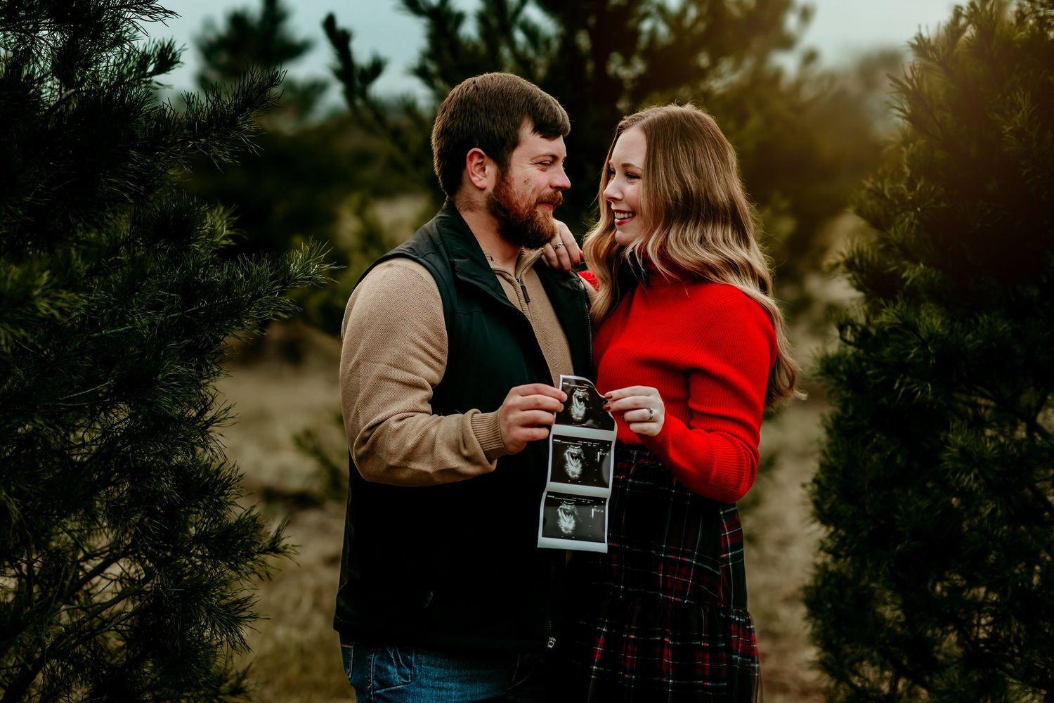 A couple holds a sonogram photo while sharing a tender moment together outdoors during golden hour.
