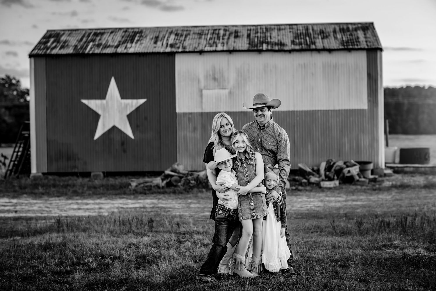 Black and white photo of a family posing in front of a Texas flag barn in a rural setting.