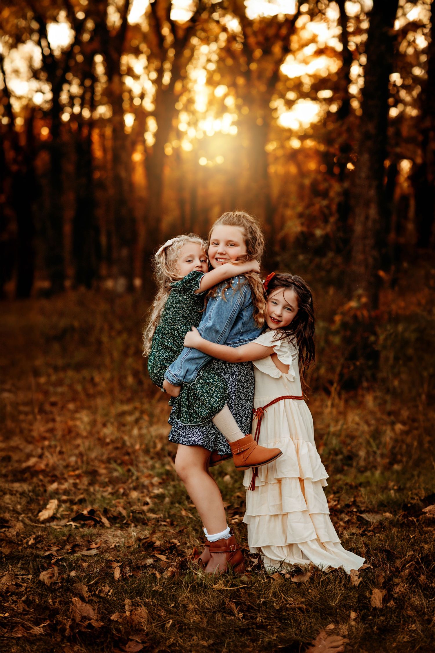 Three girls hugging and smiling in an autumn forest at golden hour sunset.