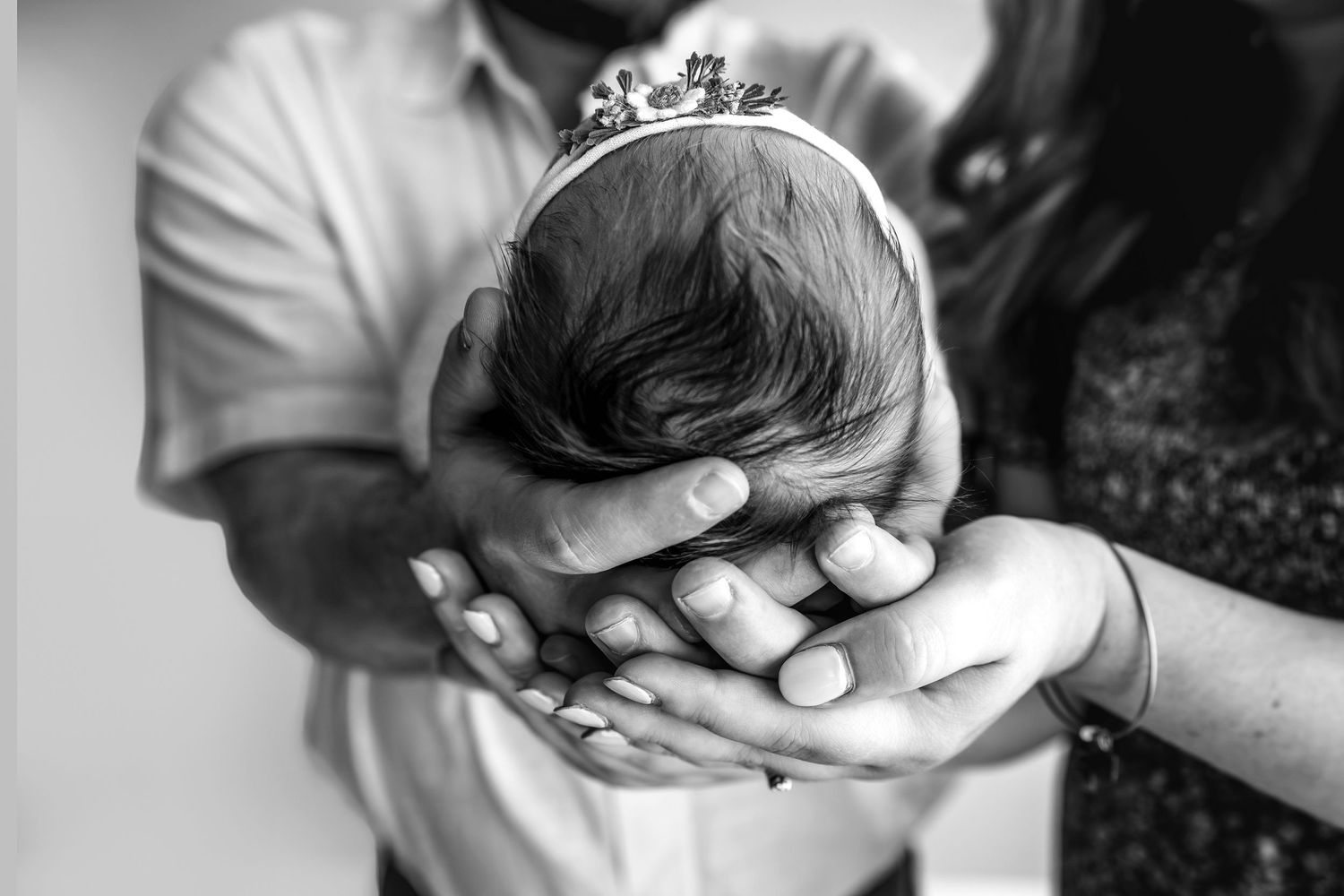 Black and white photo of parents cradling newborn baby wearing tiny crown in their hands.
