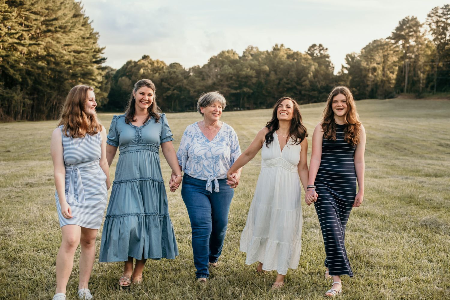 A group walks together in a grassy field at sunset wearing casual blue and white outfits.