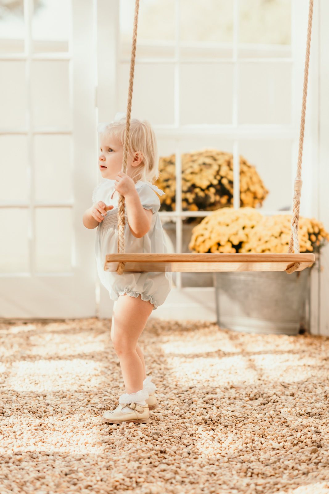 Child standing on wooden swing in sunlit room with autumn decorations.