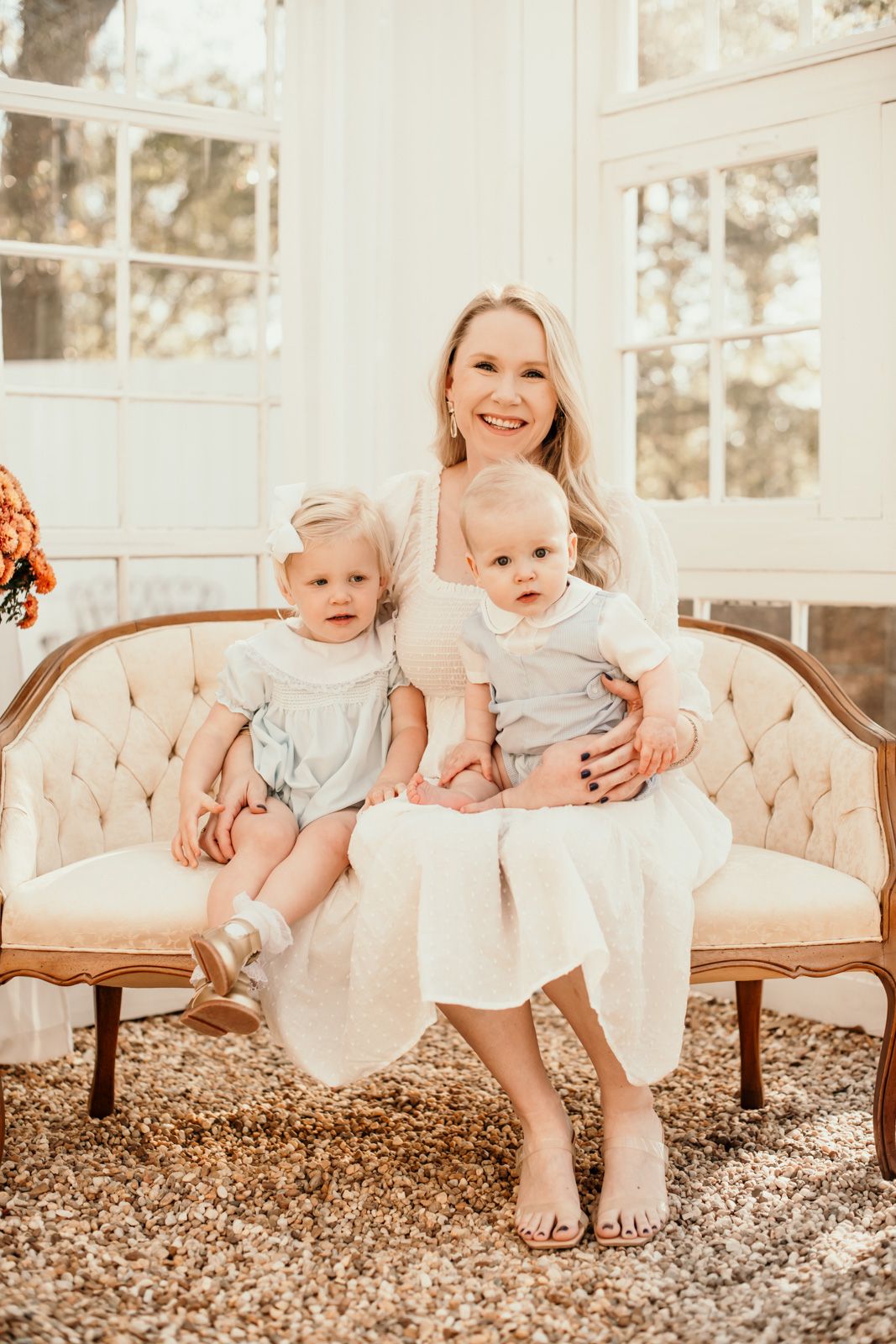 A family portrait in warm tones showing a mother and two small children sitting on an elegant vintage settee.