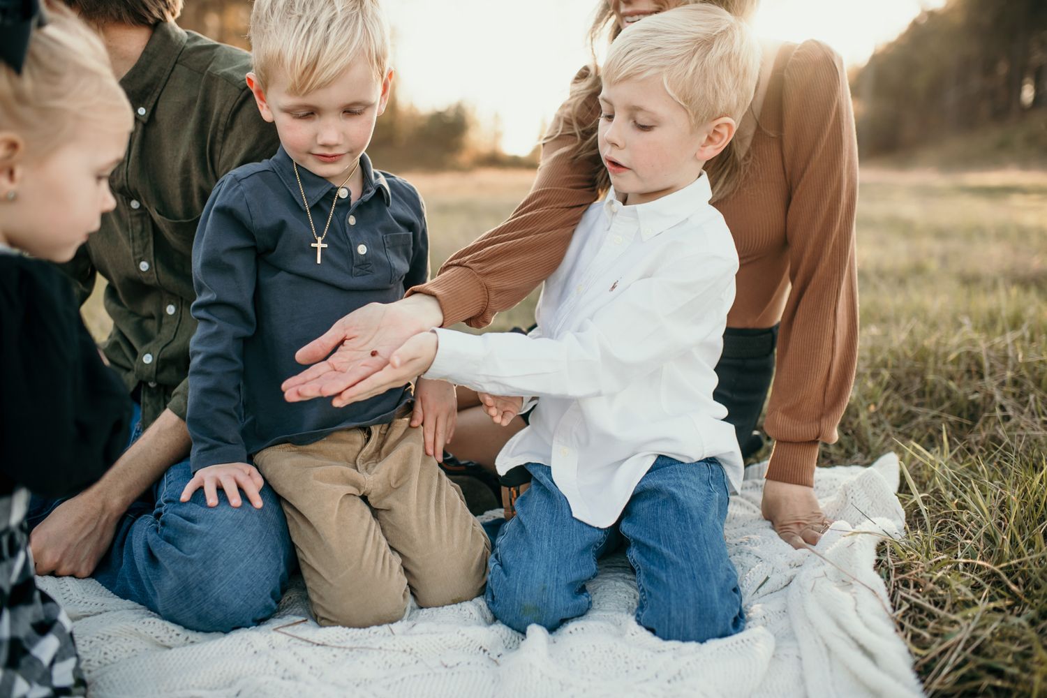 A family sits together in a golden field during sunset wearing casual denim and earth-toned clothing.