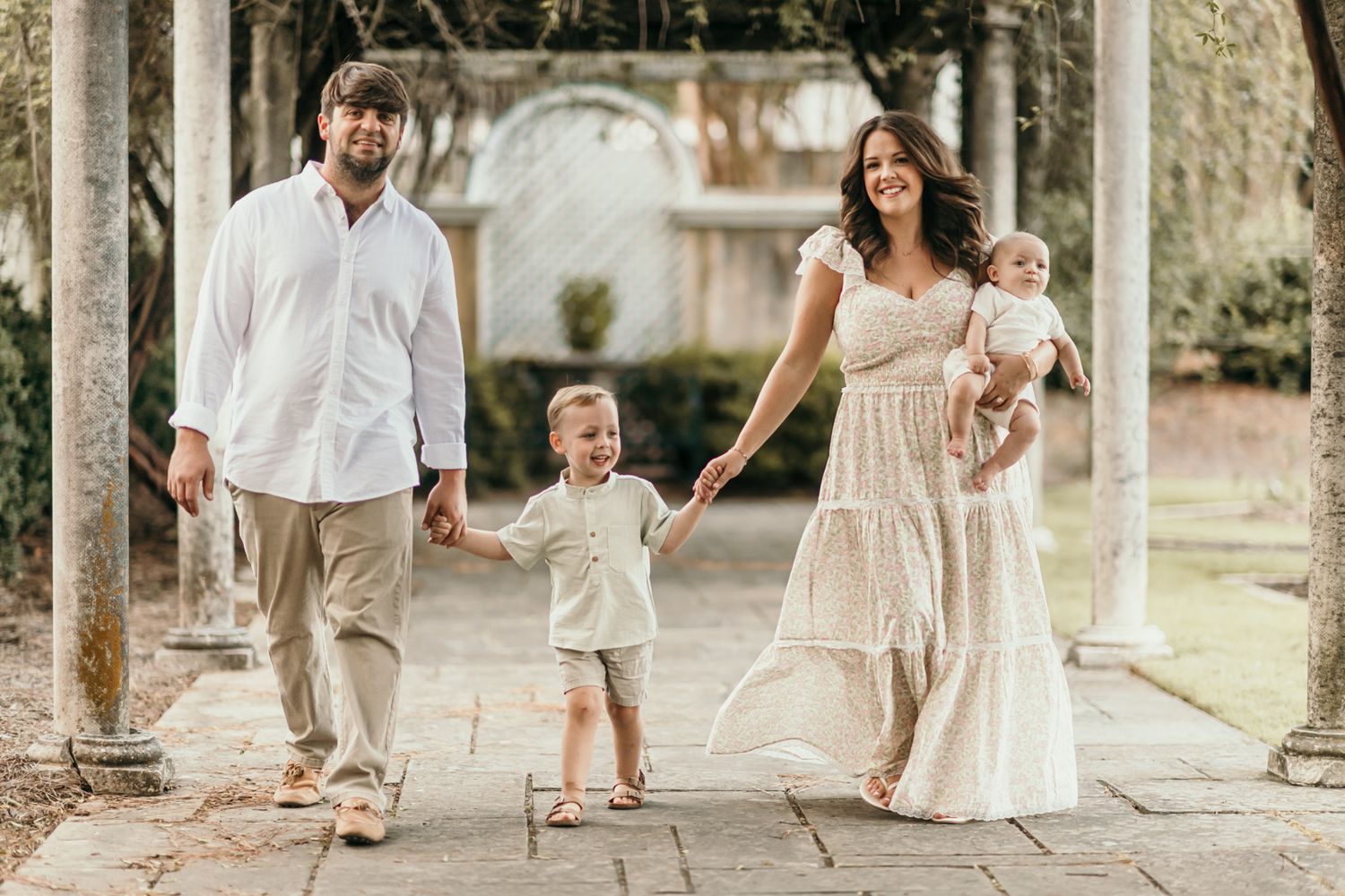 Family strolls hand in hand under an outdoor colonnade during a photo session.