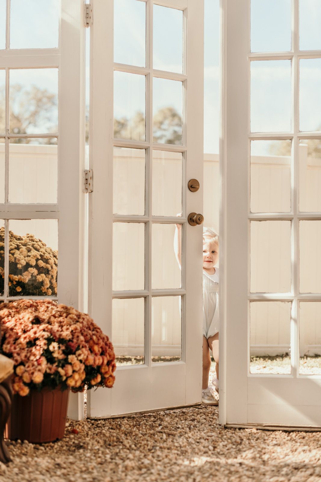 Sunlight streams through white French doors with potted mums and fall decor.
